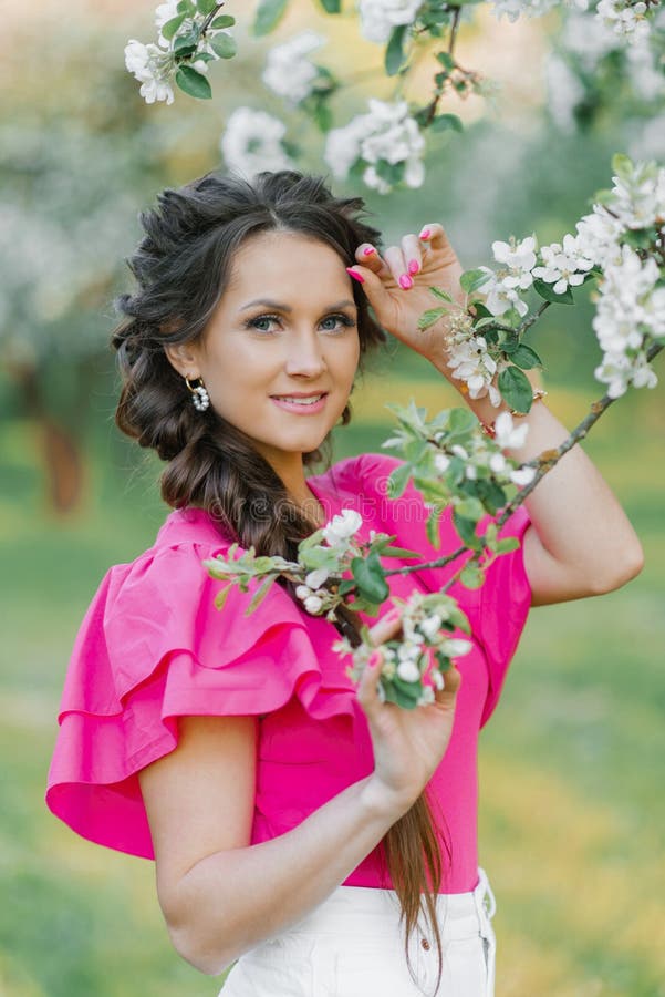 Une belle jeune européenne avec un beau maquillage et des tresses au printemps dans le parc dans un verger de pommiers en fleurs photographie stock libre de droits