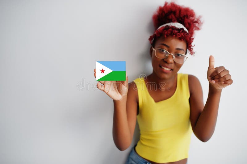 Une femme africaine aux cheveux afro vêtue d'un singet jaune et portant des lunettes porte le drapeau djiboutien isolée sur fond b. Une femme africaine aux cheveux afro porte un singet jaune et les lunettes portent un drapeau isolé sur un fond blanc montrent le pouce vers le haut.