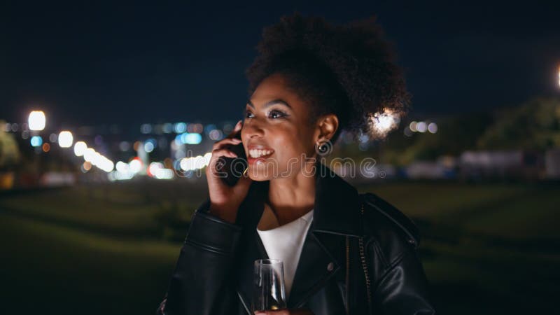 Une femme africaine qui appelle un téléphone portable tenant du wineglass la nuit dehors closeup. banque de vidéos