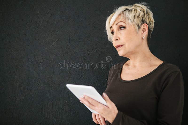 Une femme agée moderne positive réussie tient un comprimé dans des ses mains et l'emploie La génération plus ancienne et moderne photographie stock libre de droits Une femme agée moderne positive réussie tient un comprimé dans des ses mains et l'emploie La génération plus ancienne et moderne photographie stock libre de droits