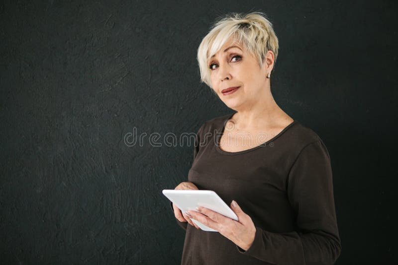 Une femme agée moderne positive réussie tient un comprimé dans des ses mains et l'emploie La génération plus ancienne et moderne images stock Une femme agée moderne positive réussie tient un comprimé dans des ses mains et l'emploie La génération plus ancienne et moderne images stock