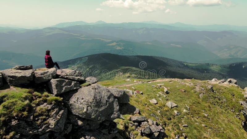 Une femme assise au sommet d'une montagne regarde au loin la beauté des montagnes carpates. vue aérienne clips vidéos