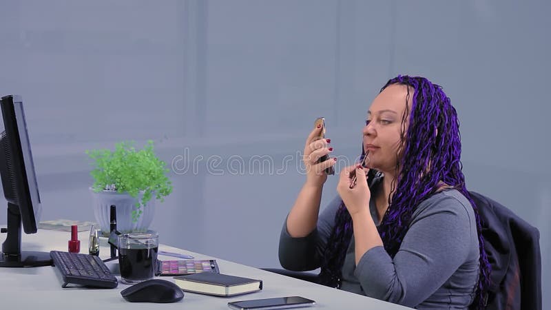 Une femme avec des tresses afro bleues dans le bureau de l'étude peint ses lèvres avec un crayon clips vidéos