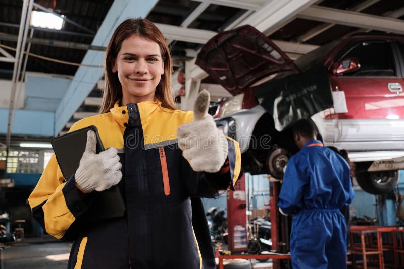 Une femme blanche travaille heureux et pouce avec le sourire dans le garage de la voiture fixe. photographie stock libre de droits