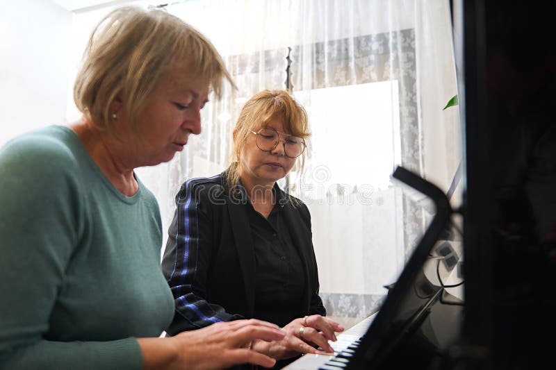 Une femme caucasienne mature enseigne à son ami à jouer du piano. leçon de musique photographie stock libre de droits