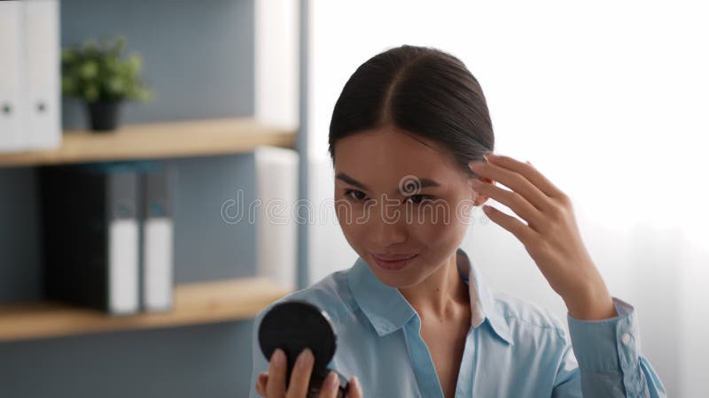 Une femme chinoise heureuse regardant un miroir assise sur le lieu de travail à l'intérieur banque de vidéos
