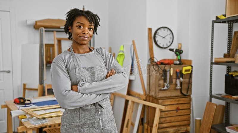 Une femme confiante avec dreadlocks se tient les bras croisés dans un atelier de menuiserie bien équipé qui dépeint habileté et pr photos libres de droits