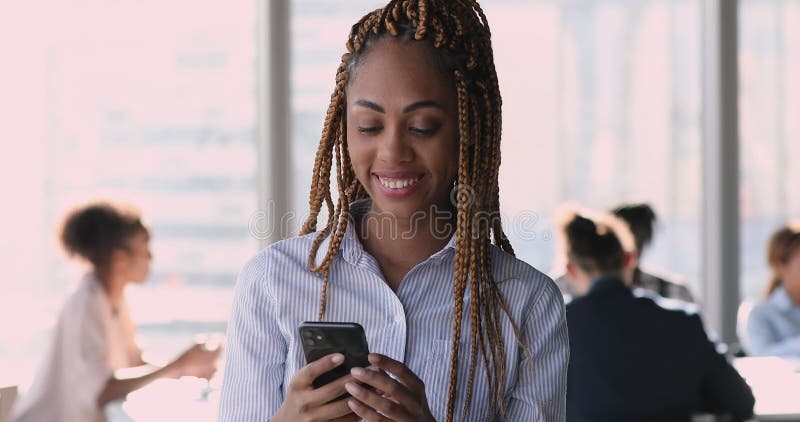 Une femme d'affaires africaine avec des tresses afro debout au travail en utilisant un smartphone banque de vidéos