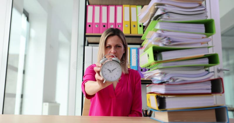 Une femme d'affaires stricte tient un réveil et de nombreux documents sur le bureau banque de vidéos