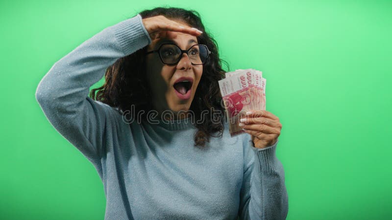 Une femme d'âge mûr qui tient des billets de couronnes islandaises regarde la distance face à un mur vert plein de curiosité et photo stock