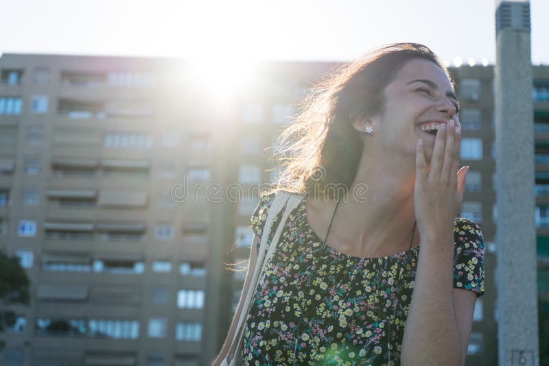 Une femme de mode riant à la bouche ouverte et la main devant dans la rue et au soleil Joyeux adolescent qui se montre dent après