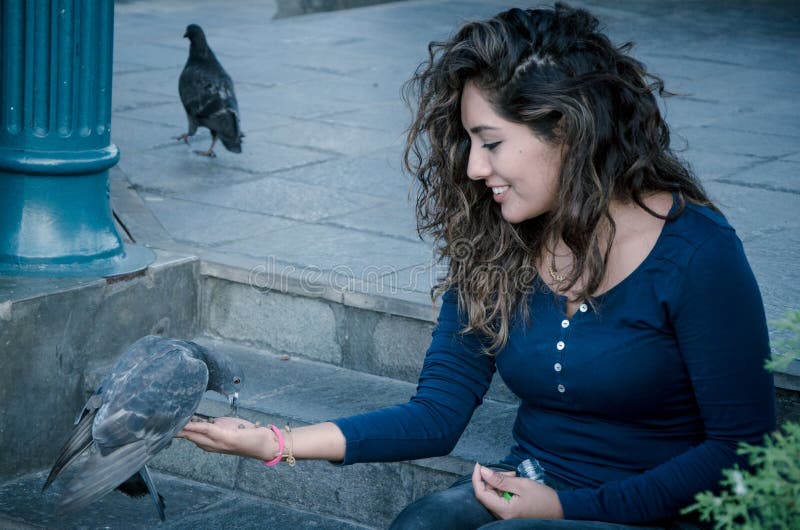 Une femme de sourire alimentant un pigeon de sa main image stock Une femme de sourire alimentant un pigeon de sa main image stock