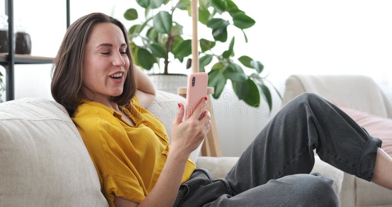 Une femme discutant en vidéo avec un téléphone portable sur un canapé à la maison clips vidéos