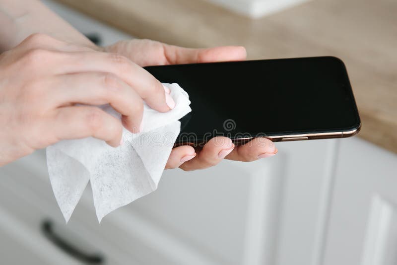 A woman wipes and disinfects a mobile phone, as a prevention of infection with influenza and Covid-19. A woman wipes and disinfects a mobile phone, as a prevention of infection with influenza and Covid-19.