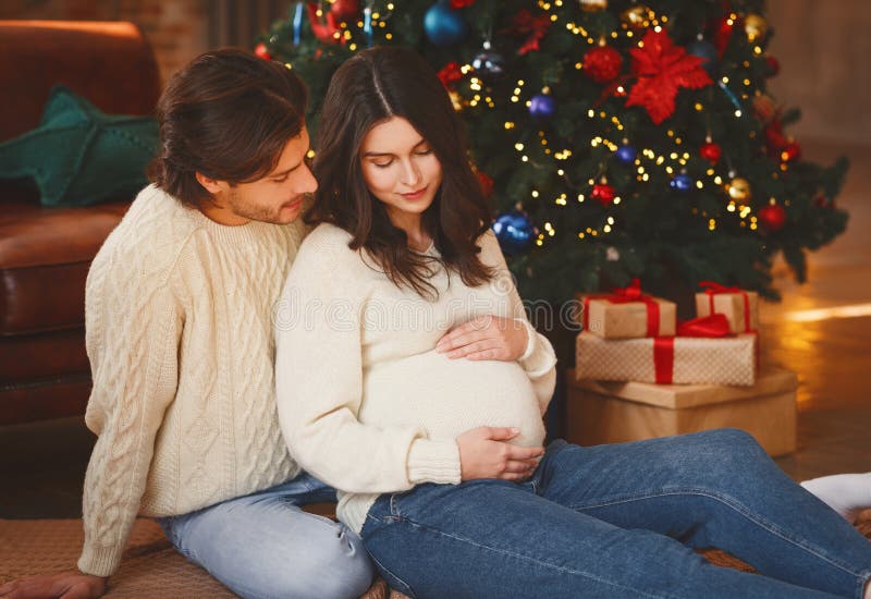 Une Femme Enceinte Assise Près D'un Arbre De Noël Avec Son Mari