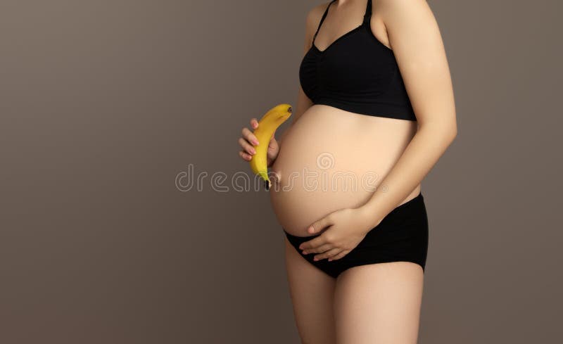 Une Femme Enceinte Se Tient Debout Dans La Pièce Et Tient De La Banane Au  Ventre. Image stock - Image du mangez, abdomen: 298442885