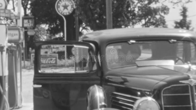 Une femme entre dans une voiture classique après avoir payé pour se remplir à la station d'essence dans les années 1930