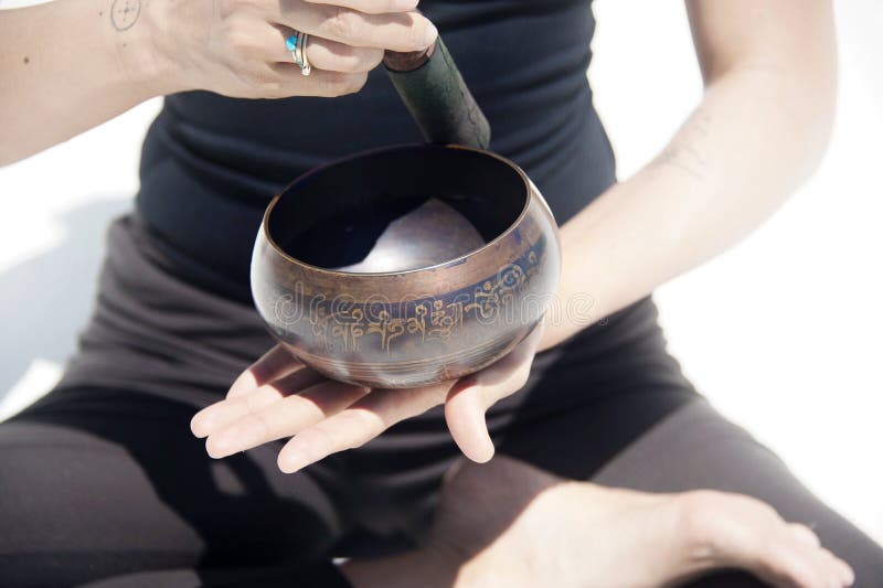 The Hands of A Sound Healing WomanSitting in Lotus Pose With Tibetan Singing Bowl photographed on a white background. This is the Ancient&#x27;s brain entrainment methodology for healing and embodied meditation. Tibetan Singing Bowls have been used for centuries for healing and meditation purposes. They create frequencies and vibrations that restore the harmony in the body, mind and spirit. Tibetan Singing Bowls:
Reduce stress and anxiety significantly.
Lower anger and blood pressure.
Improve circulation and increases blood flow.
Deep relaxation and pain relief.
Chakra balancing.
Increase mental and emotional clarity.
Promote stillness, happiness and well being. The Hands of A Sound Healing WomanSitting in Lotus Pose With Tibetan Singing Bowl photographed on a white background. This is the Ancient&#x27;s brain entrainment methodology for healing and embodied meditation. Tibetan Singing Bowls have been used for centuries for healing and meditation purposes. They create frequencies and vibrations that restore the harmony in the body, mind and spirit. Tibetan Singing Bowls:
Reduce stress and anxiety significantly.
Lower anger and blood pressure.
Improve circulation and increases blood flow.
Deep relaxation and pain relief.
Chakra balancing.
Increase mental and emotional clarity.
Promote stillness, happiness and well being.