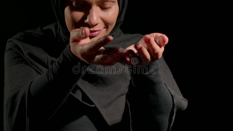 Une femme habillée en hijab noir exprime sa joie quand elle fait doucement des berceaux dans ses mains. Son sourire chaleureux con clips vidéos