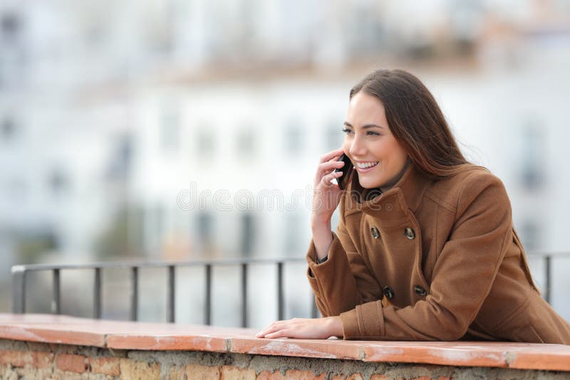 Une femme heureuse parle par téléphone sur un balcon en hiver images libres de droits Une femme heureuse parle par téléphone sur un balcon en hiver images libres de droits