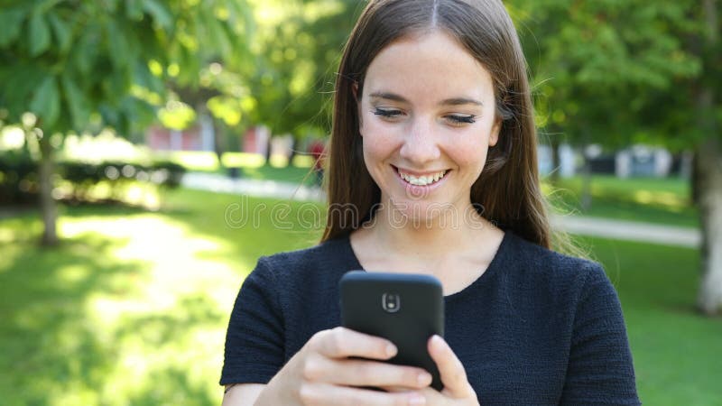 Une femme heureuse se promène dans un parc par téléphone banque de vidéos
