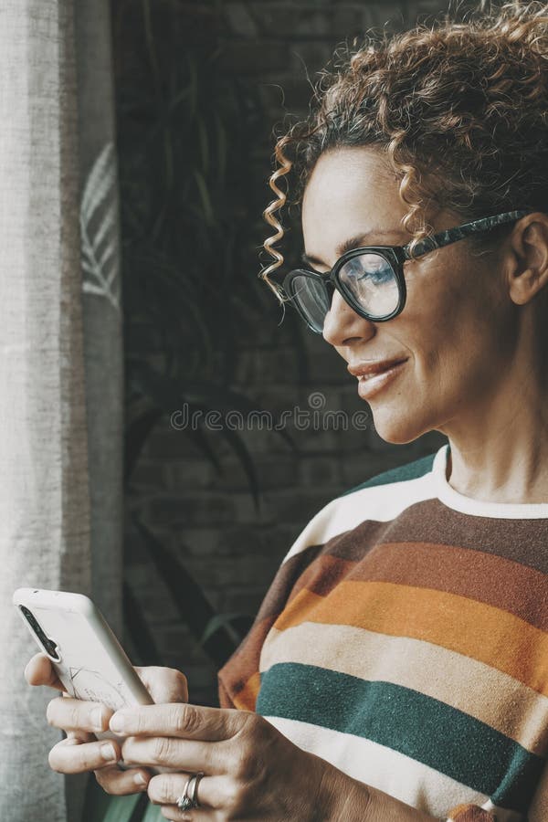 Une femme heureuse à l'intérieur souriant au téléphone et utilisant l'application pour discuter ou envoyer des messages aux gens. photos stock