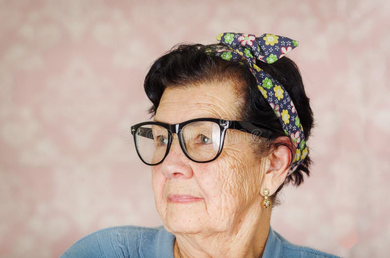 Une femme mignonne hispanique plus âgée avec l'arc de modèle de fleur sur sa tête portant le chandail bleu et les grandes lunette photo libre de droits Une femme mignonne hispanique plus âgée avec l'arc de modèle de fleur sur sa tête portant le chandail bleu et les grandes lunette photo libre de droits