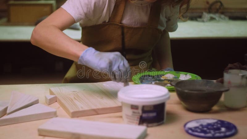 Une femme peint une partie en bois d'un produit en bois avec une brosse. idée d'entreprise pour un atelier à domicile