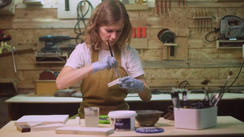 Une femme peint une partie en bois d'un produit en bois avec une brosse. idée d'entreprise pour un atelier à domicile