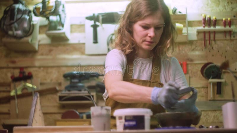 Une femme peint une partie en bois d'un produit en bois avec une brosse. idée d'entreprise pour un atelier à domicile