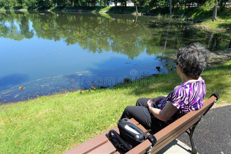 Une femme plus âgée s'assied sur le banc avec le réservoir d'oxygène regardant l'étang
