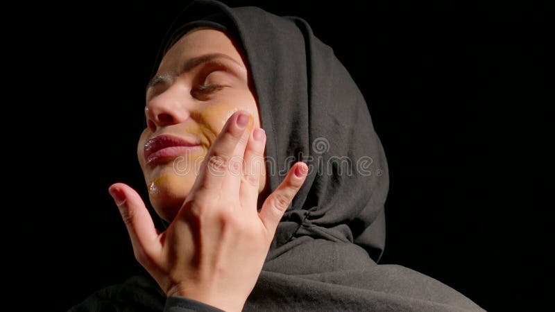 Une femme portant le hijab noir applique doucement de la crème son visage en utilisant ses doigts pour montrer sa routine de soins clips vidéos
