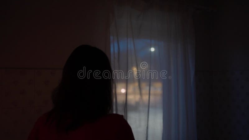 Une femme regarde par la fenêtre de sa maison en observant la scène de l'incident de nuit avec des lumières de la police hors du c banque de vidéos