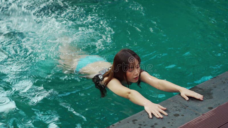 Une femme s'accroche au bord de la piscine et éclabouille d'eau avec ses pieds banque de vidéos