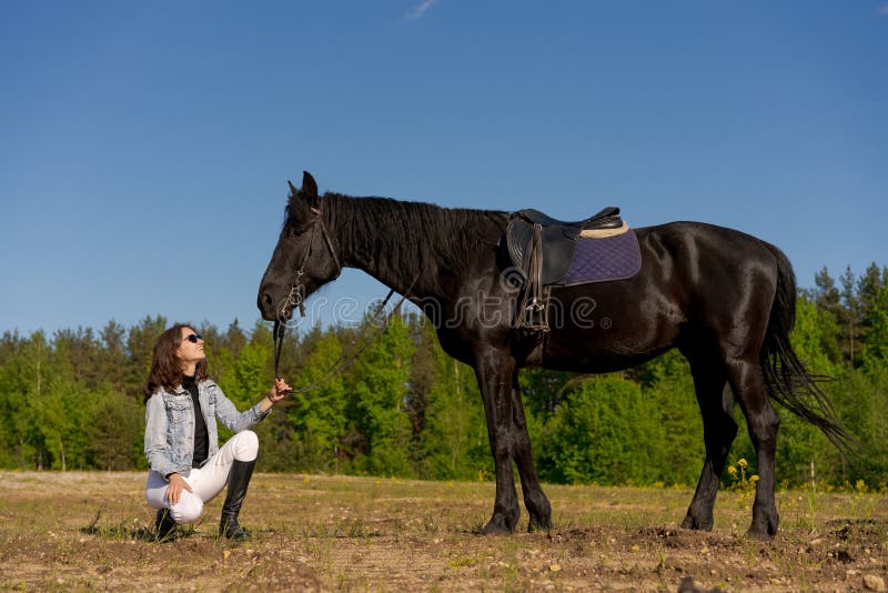 Une femme s'agenouille à côté d'un cheval noir photographie stock libre de droits