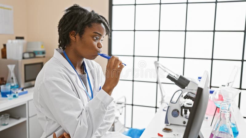 Une femme scientifique africaine réfléchie avec des dreadlocks dans un labo analyse les données dans un laboratoire moderne images stock