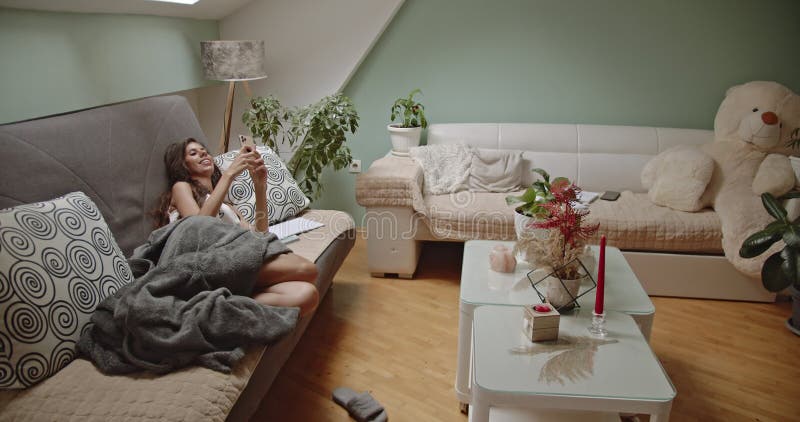 Une femme se détend sur un canapé avec un smartphone jouissant de vidéos de week-end confortables à la maison banque de vidéos