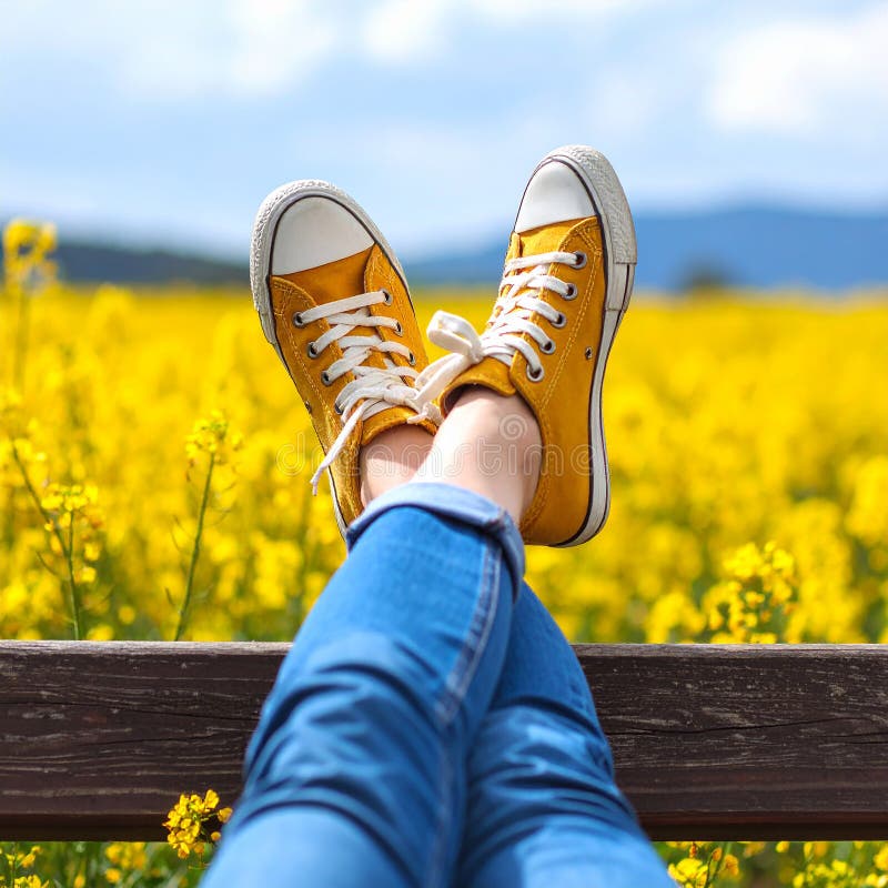 Une femme se reposant avec ses jambes soutenue sur un banc au milieu d'un champ de jaune illustration stock