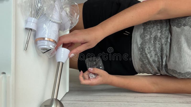 Une femme sort les composants d'un mélangeur d'immersion de l'emballage. elle examine l'appareil. vidéo verticale clips vidéos