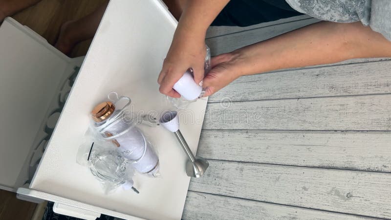 Une femme sort les composants d'un mélangeur d'immersion de l'emballage. elle examine l'appareil. vidéo verticale. large clips vidéos