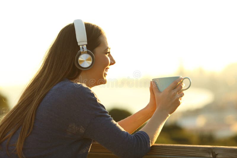 Une femme sur un balcon boit du café écoutant de la musique au lever du soleil images libres de droits