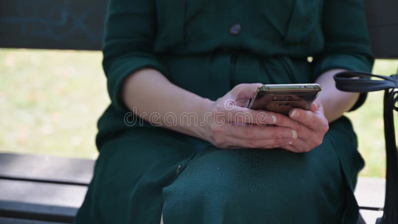 Une femme utilise un messager dans un téléphone portable tout en assis sur un banc de parc banque de vidéos