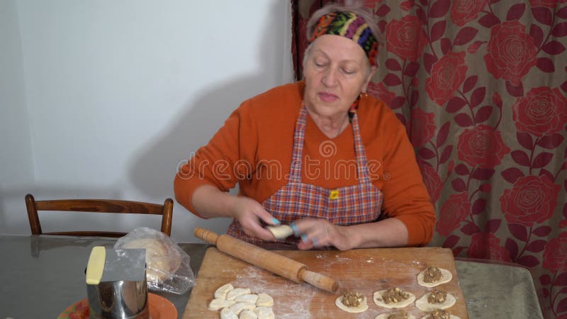 Une femme âgée fait des tartes avec de la viande. pâte maison. Grand-mère cuisine à la maison. Mains sur table de cuisine banque de vidéos