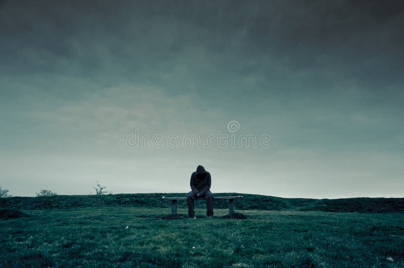 A lonely hooded figure sitting on a park bench, looking sad, lonely and depressed. With a cold, blue edit. A lonely hooded figure sitting on a park bench, looking sad, lonely and depressed. With a cold, blue edit