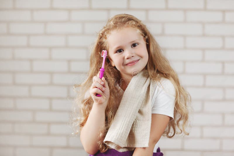 A girl with a towel on her shoulder is holding a bright pink toothbrush. Oral care, hygiene, prevention. A girl with a towel on her shoulder is holding a bright pink toothbrush. Oral care, hygiene, prevention