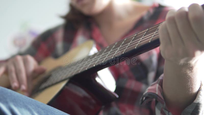 Une fille dans une chemise de plaid apprend à jouer la guitare