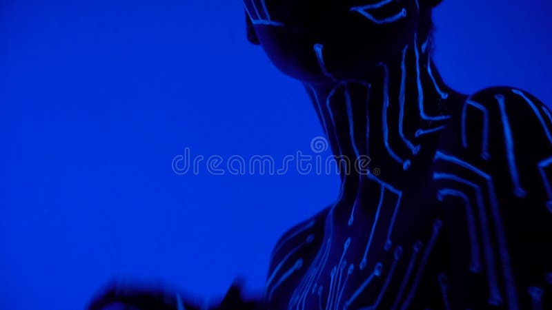 Une fille dans la lumière UV avec bodypainting sous forme de microcircuit danse dans une boîte de nuit en musique