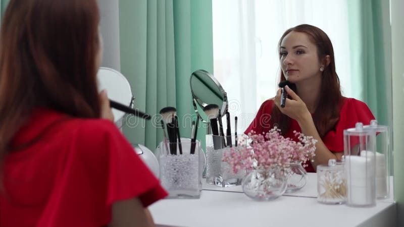 Une fille en robe de soirée lui applique de la poudre au visage. jeune femme attrayante faisant du maquillage banque de vidéos