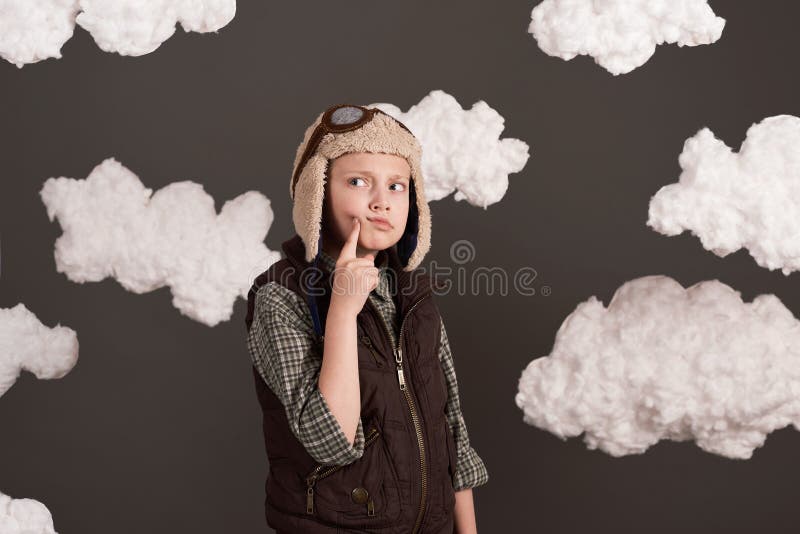 Une fille habillée dans une veste rétro et casque de style avec des verres et des rêves de devenir pilote de nuages cotonneux gris images libres de droits