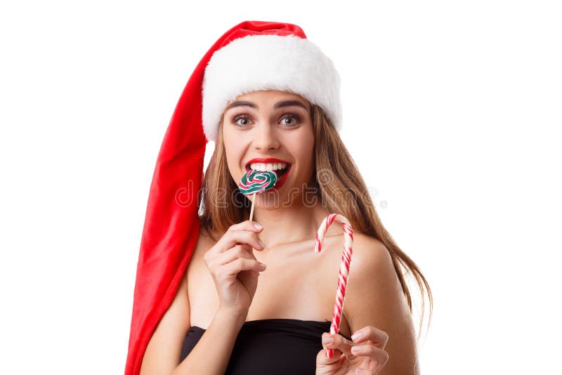 Une fille heureuse dans un chapeau de Santa tient les sucreries et les morsures colorées une de Noël de elles D'isolement sur le photographie stock Une fille heureuse dans un chapeau de Santa tient les sucreries et les morsures colorées une de Noël de elles D'isolement sur le photographie stock